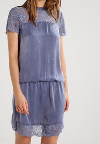 Vestido azul claro, tejido con aspecto satinado, con mangas cortas de encaje y dobladillo. Textura suave, corte holgado, cintura fruncida, intrincado patrón de encaje.