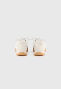 Άσπρα σουέντ αθλητικά παπούτσια με υφή φινιρίσματος, διαθέτουν ελαφριά σόλα από καουτσούκ και κορδόνια στο ίδιο χρώμα. Το λογότυπο στο πίσω μέρος είναι ορατό στη φτέρνα.