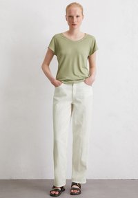 Olive green top z krótkim rękawem, luźny fason; białe, szerokie spodnie z przednimi kieszeniami; czarne płaskie sandały z paskami i detalem z klamrą.