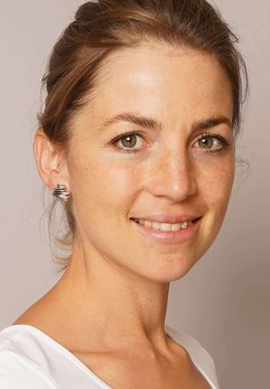 Silberne Spiral-Stiftohrringe mit polierter Oberfläche, die ein geschichtetes Design und subtile Textur aufweisen, getragen von einer Frau vor einem neutralen Hintergrund.