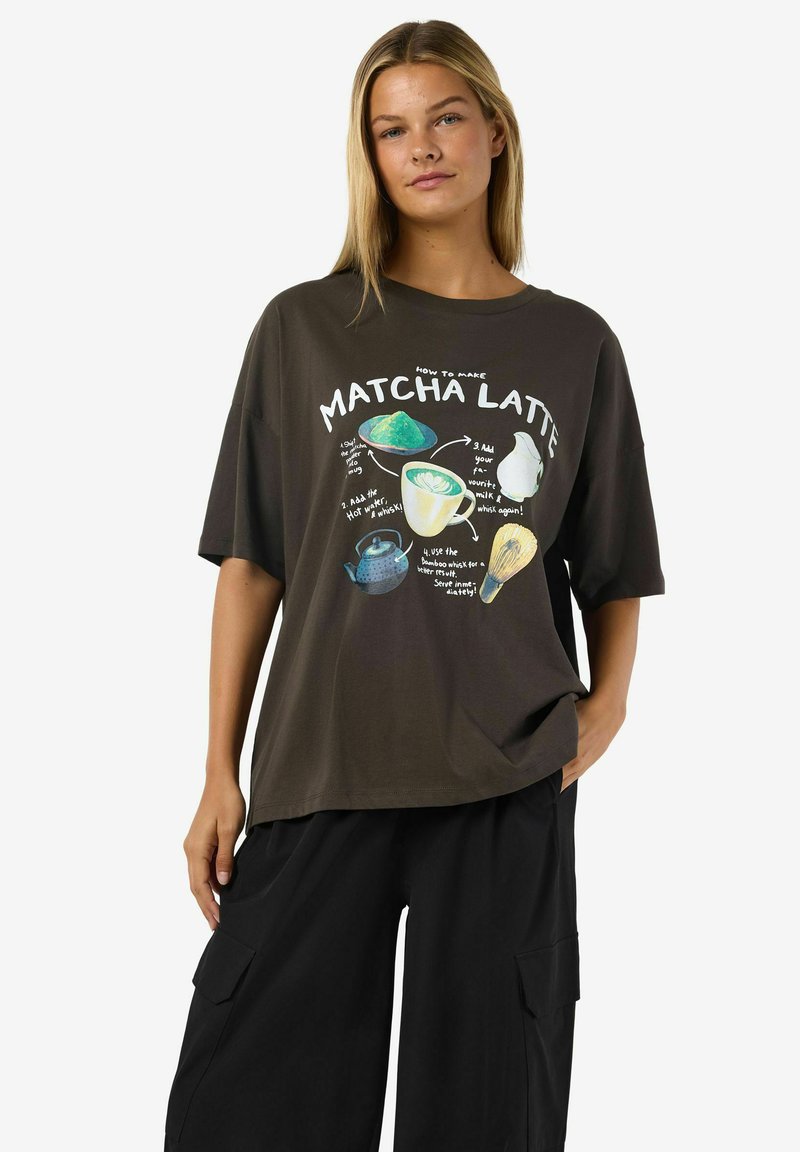 Tamno smeđa oversized majica s grafikom recepta za matcha lattea, sa šarenim ilustracijama sastojaka i pribora.