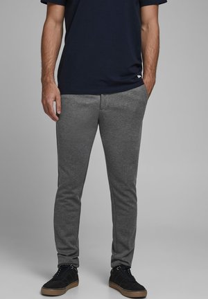 Szare spodnie sportowe o slim fit z elastycznym pasem, wykonane z gładkiego materiału. W połączeniu z czarnymi trampkami i granatową koszulką.