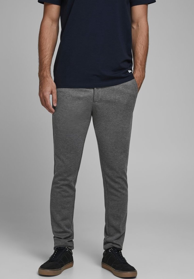 Šedé sportovní kalhoty s úzkým střihem a elastickým pasem, vyrobené z hladké látky. V kombinaci s černými teniskami a námořnickým tričkem.