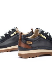Black leather shoes with brown accents, textured gray laces, side zippers, and rugged rubber soles. Features Pikolinos branding.