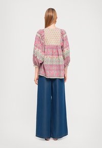 Blusa a maniche puff con motivo floreale in verde chiaro e rosa, con design a peplo, abbinata a pantaloni in denim a gamba larga di colore blu scuro.