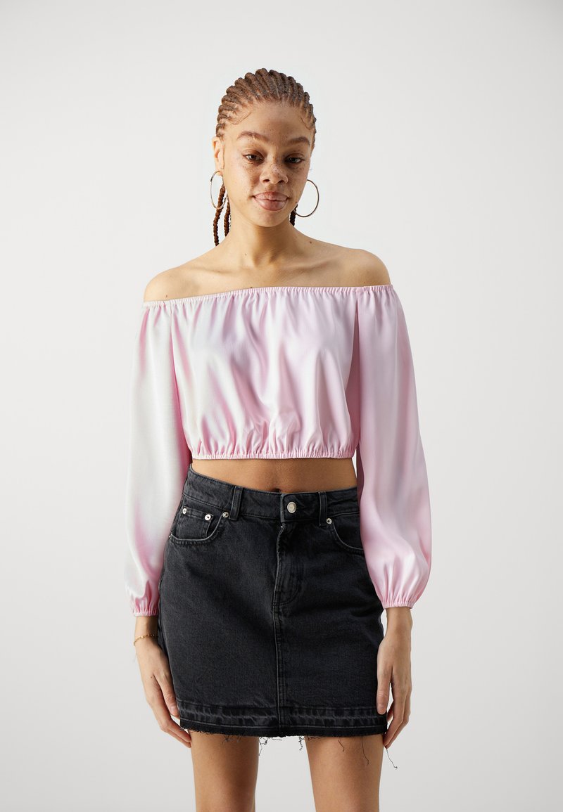 Top in satin rosa chiaro asimmetrico, con orlo arricciato, abbinato a una mini gonna in denim nera con orlo sfrangiato e tasche frontali.