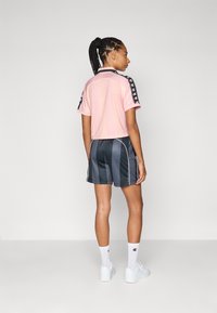 Camiseta atlética de manga corta rosa con acentos de logo negros, combinada con pantalones cortos a rayas horizontales gris oscuro y calcetines blancos jusqu al tobillo.