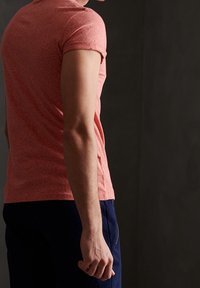 T-shirt med kort ärm, åtsittande i texturerat koralltyg, i kombination med marinblå byxor. Utsikten visar ryggen med lätt synlighet av axlarna.