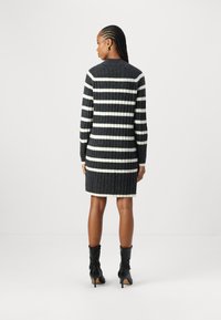 Robe en tricot avec une texture côtelée, ornée de rayures verticales noires et blanches, à manches longues et coupe au genou. Bottes noires à hauteur de genou.