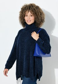 Maglione oversize blu navy con collo alto e finitura testurizzata, abbinato a una piccola borsa blu strutturata e jeans in denim.