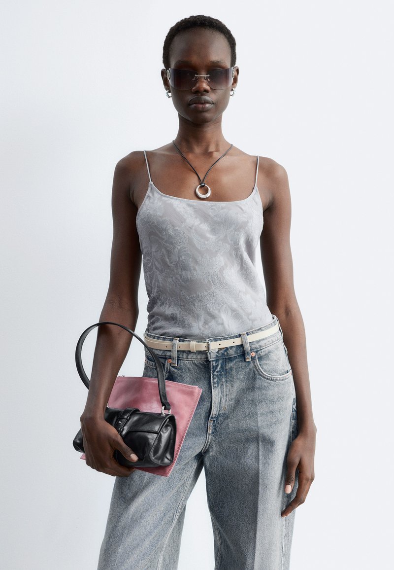 Femme portant un caraco en satin argenté, un jean taille haute, des lunettes de soleil, un collier pendentif rond, tenant deux sacs à main—un noir, un rose.