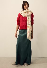 Red cable-knit sweater, cream scarf with colorful patterns, green satin maxi skirt, and woven flats. Simple and layered combination.
