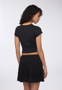 Top corto a costine nero con maniche corte abbinato a una gonna nera a strati con dettagli arricciati e vita elastica.