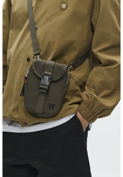 Sac bandoulière vert olive avec rabat arrondi, sangle ajustable, fermeture éclair et logo en accent. Fabriqué en nylon avec une texture lisse.