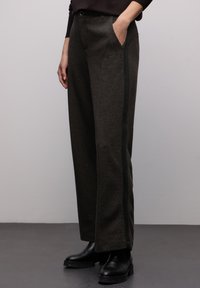 Ciemnobrązowe, dopasowane spodnie o fakturowanym wzorze, wyposażone w boczne kieszenie i subtelny czarny pasek wzdłuż boku. Gładkie wykończenie materiału.