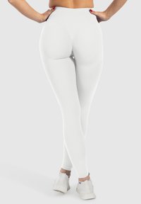 Leggings bianchi a vita alta con un design aderente, texture liscia e tessuto elasticizzato, abbinati a scarpe da ginnastica bianche.