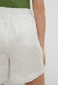 Weiße Leinenshorts mit einem elastischen Bund, die einen lockeren Schnitt und leicht umgeschlagene Säume für einen lässigen Look bieten.