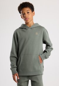 Grüne Kapuzenjacke aus weichem Stoff mit einer vorderen Kängurutasche und einem kleinen Logoschild. Lange Ärmel mit gerippten Bündchen.