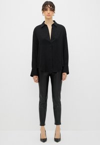 Camicia nera con bottoni e un sottile motivo leopardato, maniche lunghe e colletto, abbinata a pantaloni in pelle nera lucida e tacchi a punta neri.