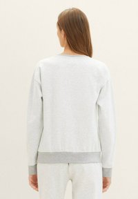 Sudadera gris claro con cuello redondo, mangas largas y puños y dobladillo acanalados. La tela parece suave con una textura lisa.