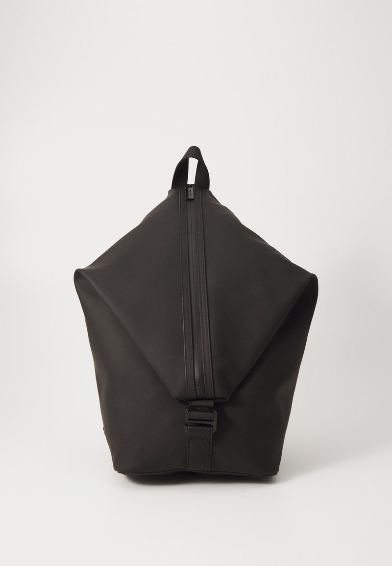 Černý batoh s geometrickým designem, vyrobený z hladkého materiálu. Obsahuje centrální zip a horní rukojeť pro nošení.