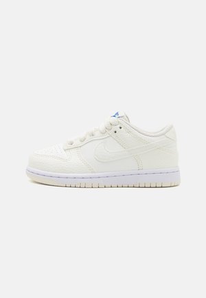 Weißer Low-Top-Sneaker aus strukturiertem Leder, mit perforierter Spitze, Schnürsenkeln und einem blauen Logo auf der Zunge, von der Seite auf weißem Hintergrund gezeigt.