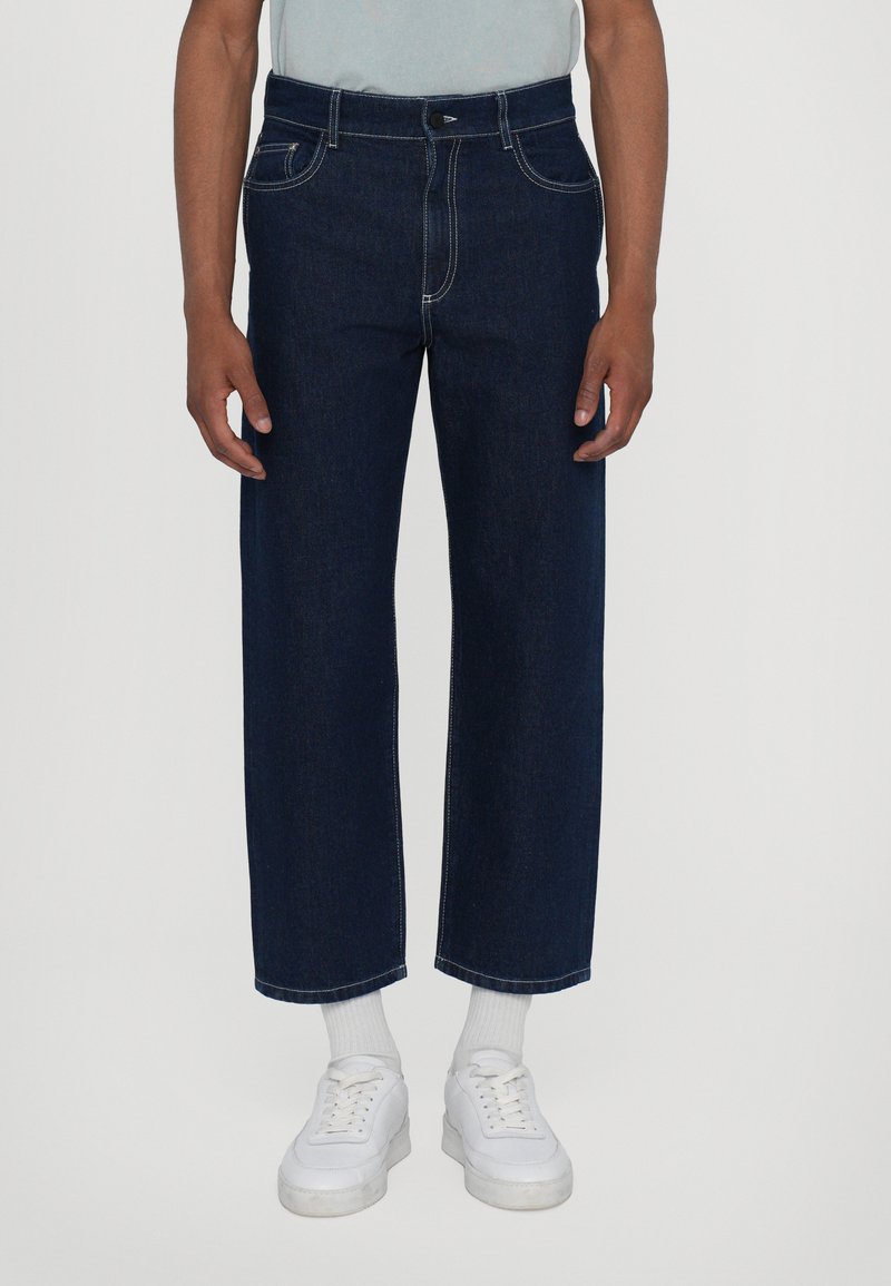 Jeans in denim blu con una vestibilità rilassata, gamba dritta, cuciture bianche a contrasto, cinque tasche e chiusura a bottone in vita.