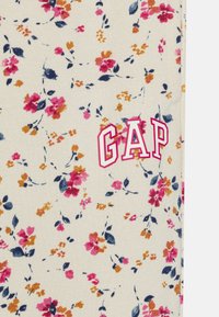 Ziedu audums ar rozā, apelsīnu un jūras bruņurupuča krāsas ziediem uz krēma fona. "GAP" logo biezās rozā kontūrētās burtiem.