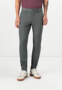 Szürke, szabott nadrág texturált anyagból, slim fit szabással és kontrasztos oldalsávokkal, fehér sportcipőkkel párosítva.