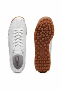 White athletic shoes with a smooth leather upper, lace closure, and a gum rubber sole featuring circular traction points. Logo visible on the tongue.