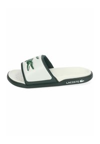 Chanclas de Lacoste en blanco y verde oscuro con el logo de cocodrilo en la correa y el nombre de la marca en el lateral de la suela.