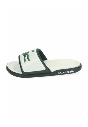 Chanclas de Lacoste en blanco y verde oscuro con el logo de cocodrilo en la correa y el nombre de la marca en el lateral de la suela.