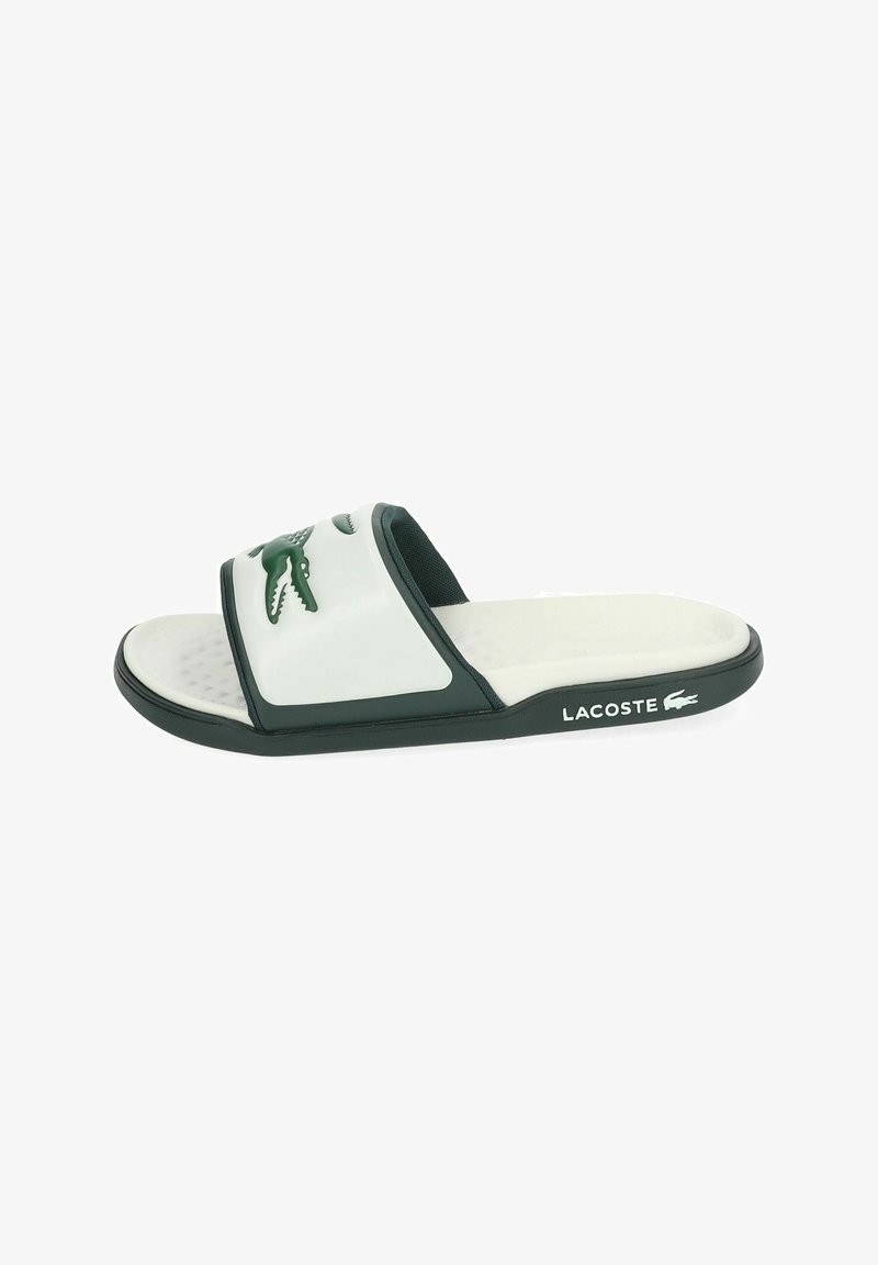 Chanclas de Lacoste en blanco y verde oscuro con el logo de cocodrilo en la correa y el nombre de la marca en el lateral de la suela.