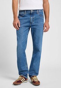 Jean azul de mezclilla con corte recto, cinco bolsillos y cierre de botón. La tela tiene un aspecto texturizado y ligeramente deslavado.