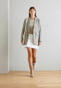 Ljust grå rutigt kavaj, beige topp, vit denimkjol med knappar och fransad nederkant, samt tan slouchy stövlar. En enkel handväska fulländar looken.