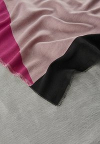 Geweven deken met een roze, bordeauxrode en zwarte kleurblokontwerp, voorzien van een gestructureerde afwerking en franjes langs één rand.