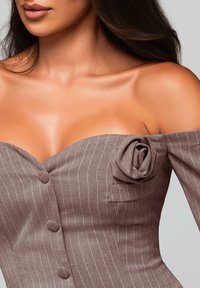 Femme portant une robe marron à rayures fines décolletée avec un détail de rose en tissu, des boutons sur le devant, et laissant apparaître la clavicule et la partie supérieure de la poitrine.