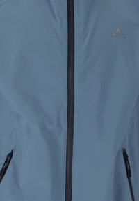 Ljusblått vattentätt jacka med full frontdragkedja, svarta dragkedjedetaljer och sidofickor med dragkedja. Har en triangulär logotyp på bröstet.