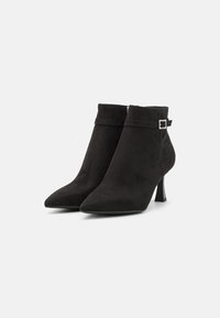 Bottes chevilles en suède noir avec un bout effilé, un talon moyen et une sangle décorative avec un petit accent de boucle carrée.
