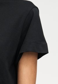 Λεπτομέρεια μανσετών μαύρου κοντομάνικου πουκάμισου σε άτομο με ανοιχτό καφέ δέρμα σε απλό ανοιχτό φόντο.