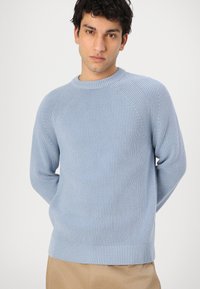 Pull en tricot côtelé bleu clair avec un col rond et des manches raglan, présentant un motif texturé et une taille ajustée.