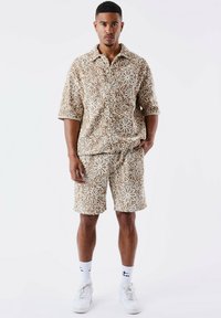 Conjunto de camiseta de manga corta y pantalones cortos en una tela beige con bordado floral blanco; ajuste relajado, diseño con cuello, y combinar con zapatillas blancas.