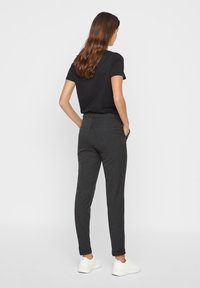 Pantaloni grigi scuri su misura con una vestibilità slim, tasche frontali e una superficie liscia, abbinati a una maglietta nera a maniche corte e sneakers bianche.