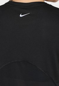Camiseta atlética negra con un panel de malla en la parte inferior y un pequeño logo blanco de Nike en la parte posterior cerca del escote.