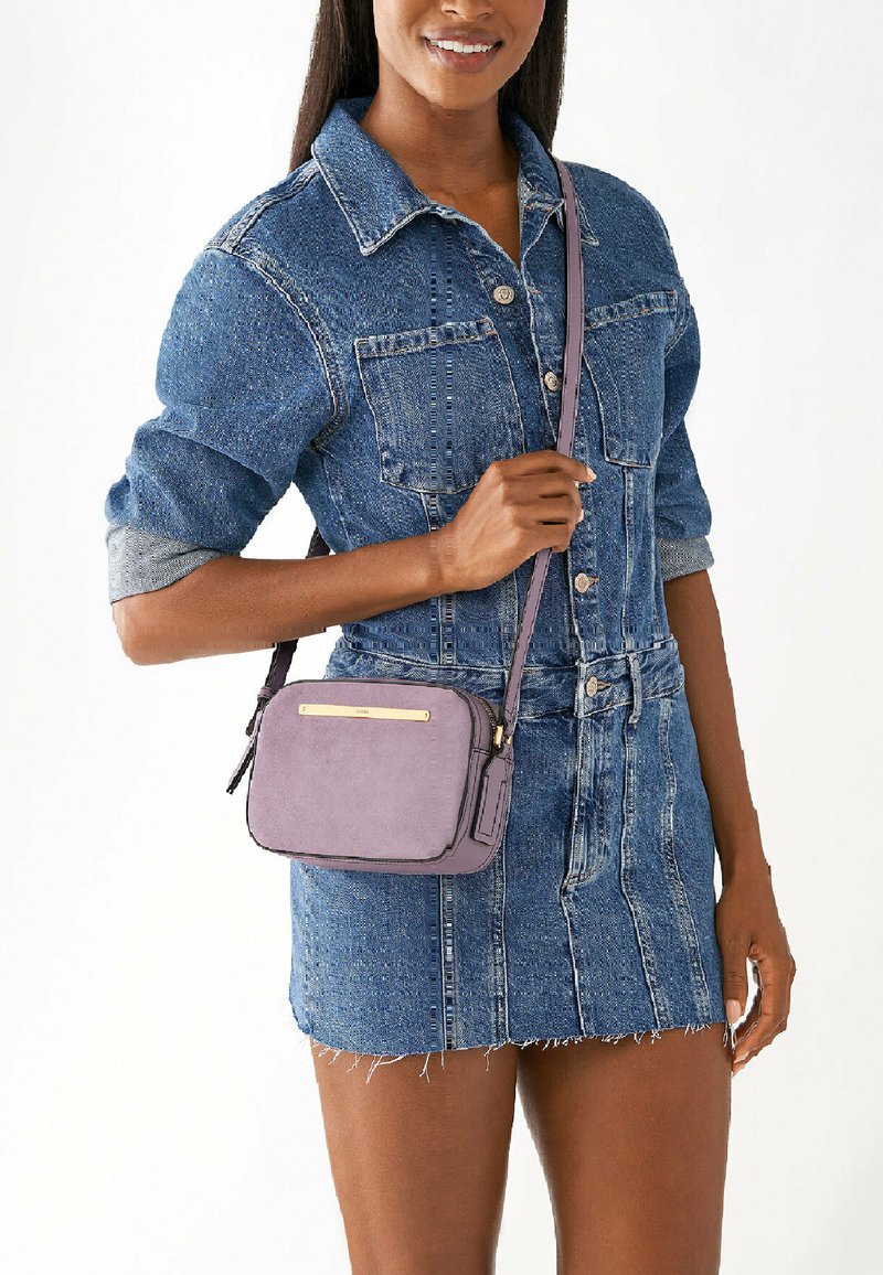 Borsa a tracolla viola con finitura a superficie liscia, accessori in oro, forma rettangolare e tracolla regolabile, esposta su un tessuto di denim.