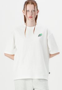 T-shirt blanc surdimensionné en coton doux, avec des manches courtes et un logo brodé multicolore sur la poitrine.