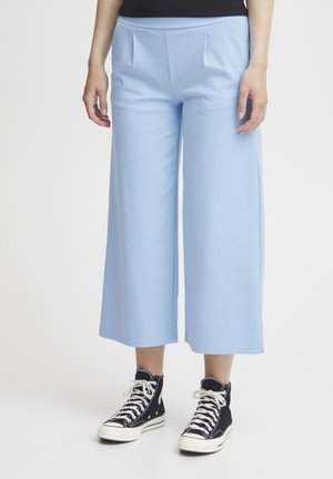 Pantaloni a gamba larga azzurro chiaro realizzati in morbido tessuto, con una texture liscia e pieghe frontali, abbinati a sneakers nere alte.