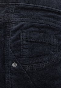 Donker denim stof heeft een gestikte achterzak met een metalen klinknagel en subtiele textuur, wat de kwaliteit en het ontwerp van het materiaal benadrukt.