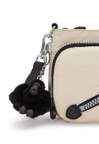 Beżowa torebka na ramię z tkaniny z czarnymi zamkami błyskawicznymi i dodatkami. Posiada odpinany czarny futrzany brelok w kształcie goryla przy suwaku. Zawiera srebrne elementy ozdobne.