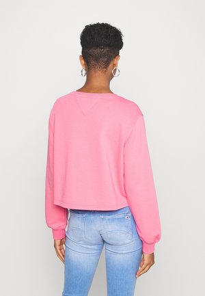 Sweatshirt rose cropped à manches longues, avec un col rond et des poignets côtelés. Texture de tissu lisse, détails de couture minimalistes au dos.